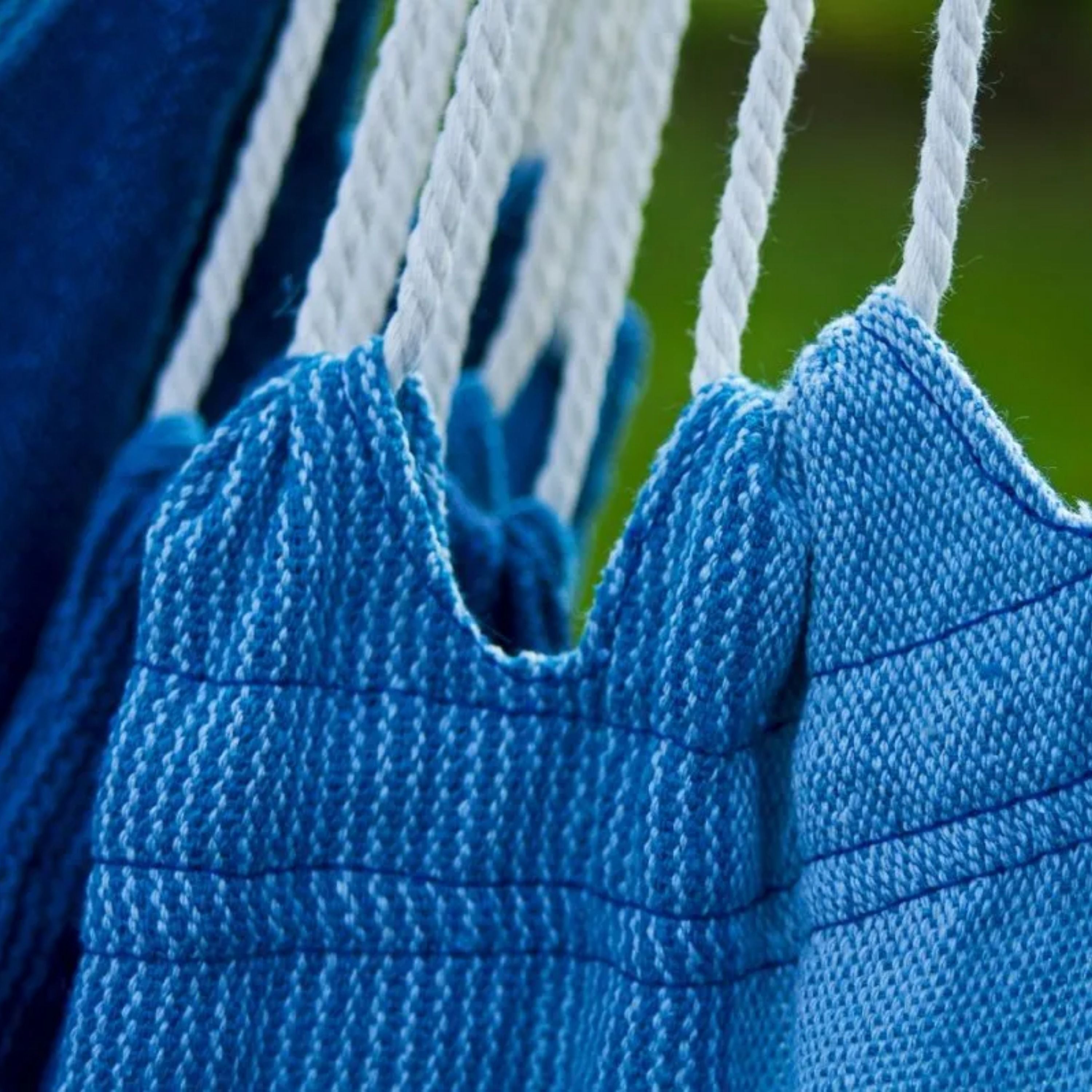 Zoom sur le fauteuil suspendu bleu Horizonte de chez Hamacio dans un jardin