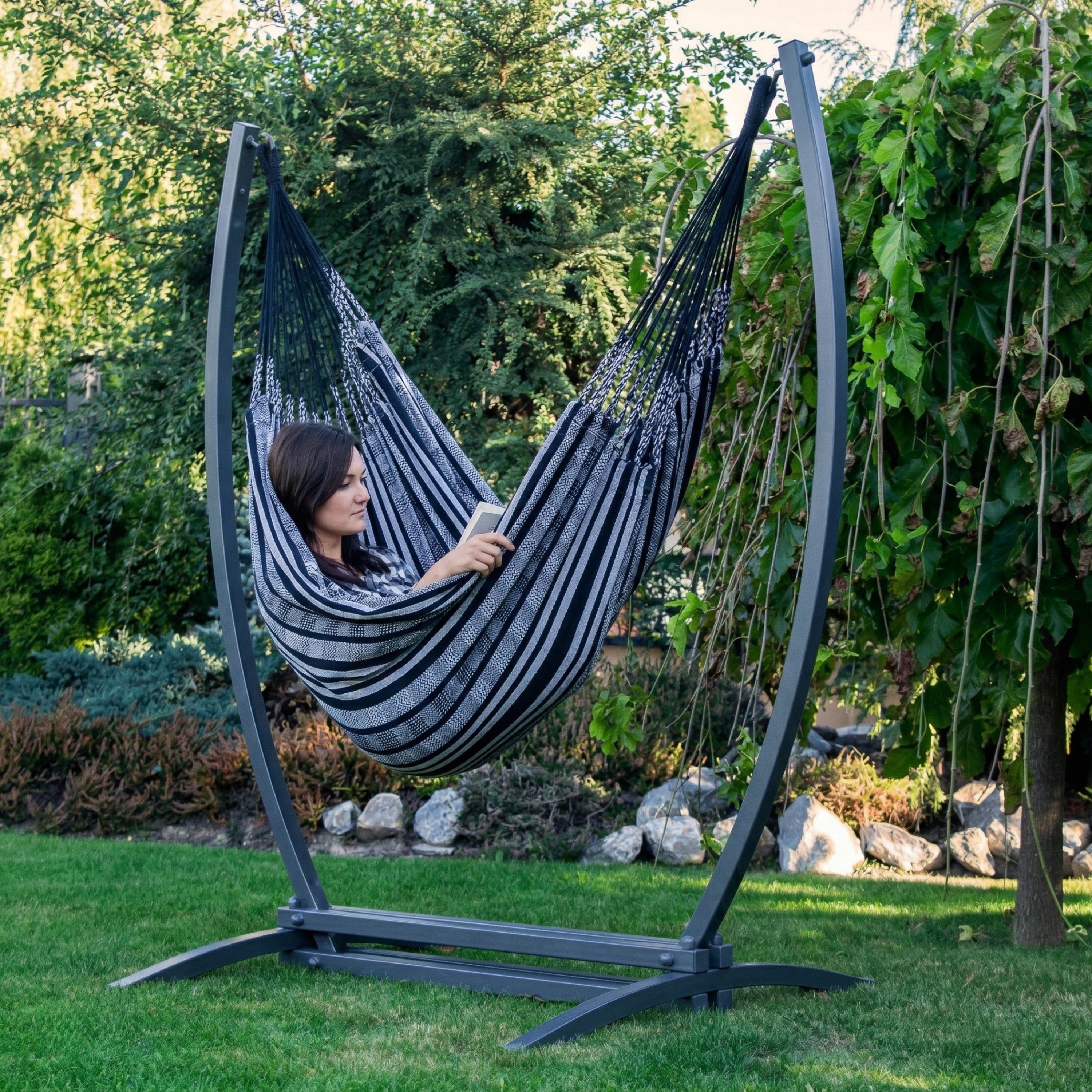 Hamac suspendu noir de hamacio dans un jardin avec une femme assise en train de lire un livre 